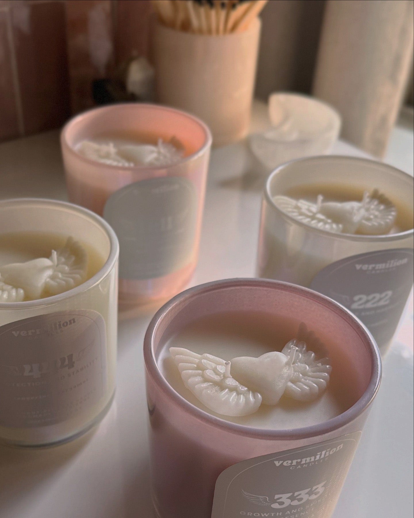 Candles in pink and gray containers with decorative elements on a light surface.